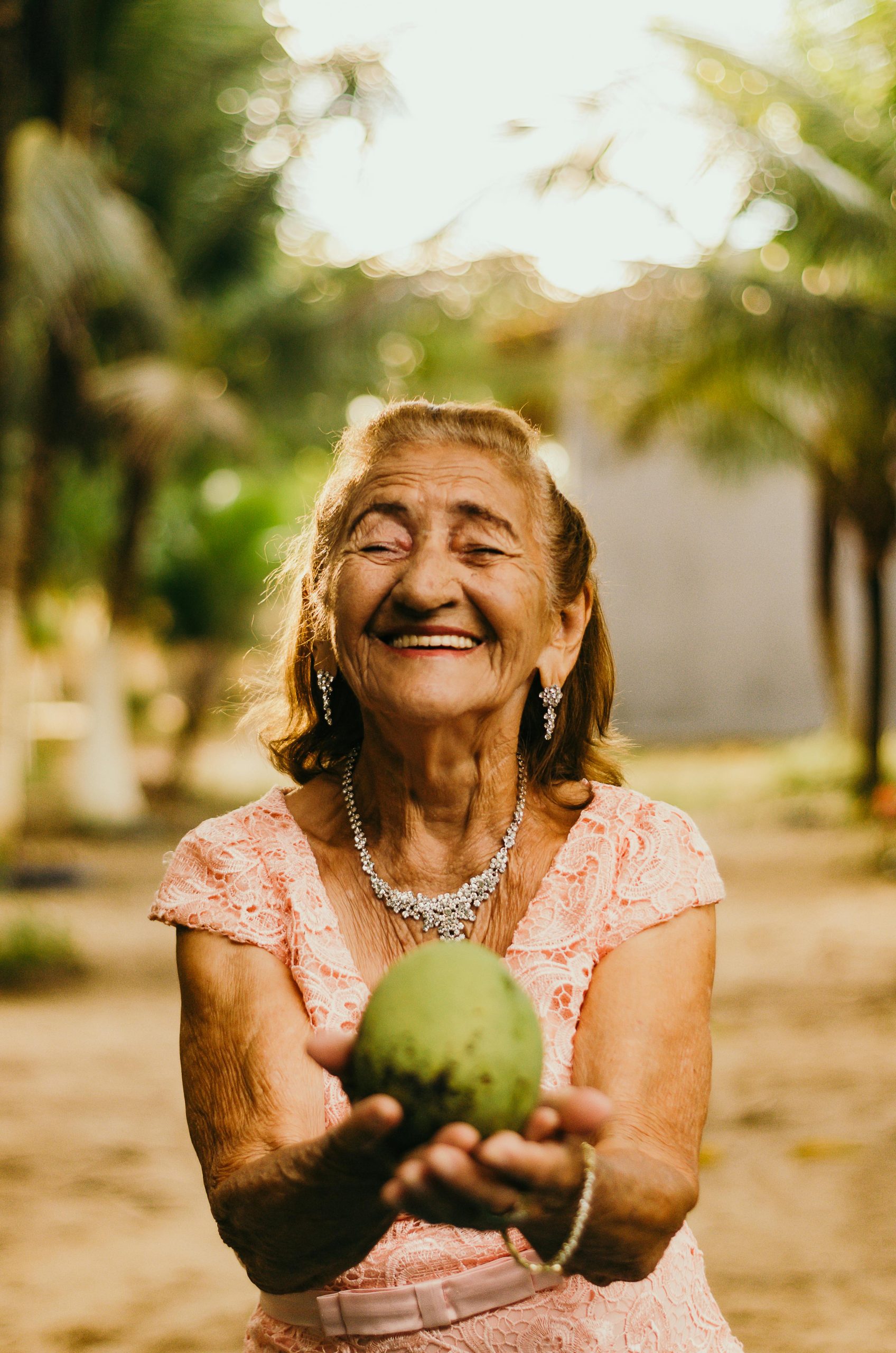 smiling-senior-woman-white-teeth Smiling senior woman necklace white teeth offering a fruit