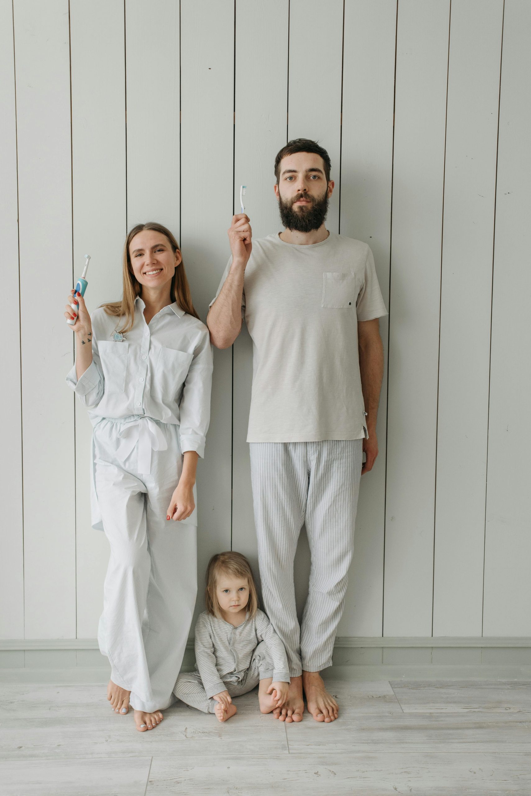 Family smiling on wall holding toothbrush.