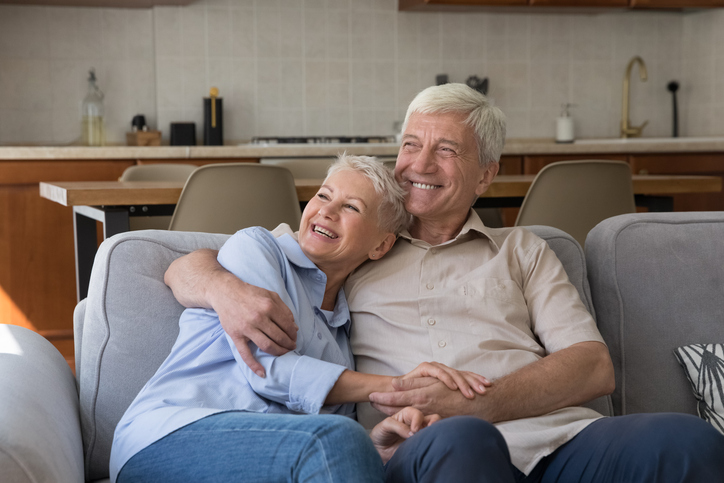 Healthy happy old couple pensioners cuddle on sofa look at distance dream spend good days together on retirement. Loving affectionate mature husband wife rest on couch imagine visualize future plans Senior couple embracing and smiling on couch